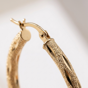 14K yellow gold oval hoop earring, macro detail of diamond-cut satin texture and hinged clasp
